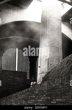 Kontrastreiches Schwarz-weiß-Architekturfoto mit einer hohen zylindrischen Ziegelsäule neben geschwungenen Ziegelbögen und perforierten Gittern Stockfoto