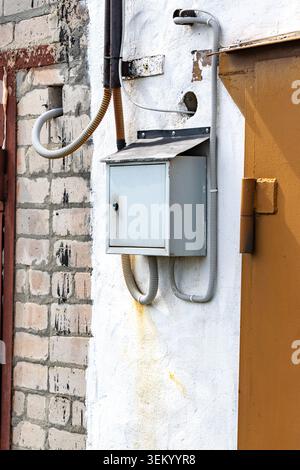 Eine rustikale, an der Wand montierte Mailbox mit einer Kabelverbindung über Kopf, die bei natürlichem Licht gegen eine strukturierte Ziegeloberfläche erfasst wird Stockfoto