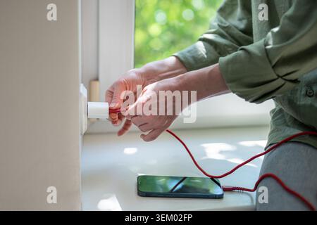Frau, die ein beschädigtes Telefonladekabel anschließt und versucht, das Smartphone aufzuladen, steckt die Steckdose an Stockfoto