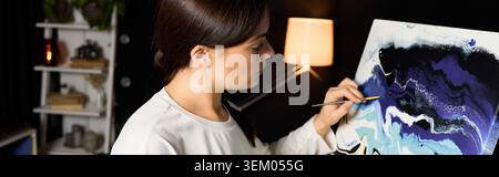Die junge Frau malt leidenschaftlich farbenfrohe abstrakte Kunst in ihrer warmen und einladenden Umgebung. Stockfoto