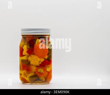 Ein Gefäß steht auf einer glatten Oberfläche, gefüllt mit einer Vielzahl von gemischtem Gemüse, genannt Chow Chow. Zu den Gemüsesorten gehören Karotten, Blumenkohl und Paprika. Sie werden in einer klaren Salzlake aufbewahrt. Stockfoto