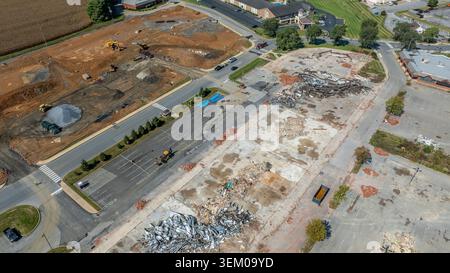 Arbeiter sind an Bau- und Abbrucharbeiten auf einem Parkplatz beteiligt. Es sind schwere Maschinen vorhanden, und Gebäude werden gerade abgenommen. Stockfoto