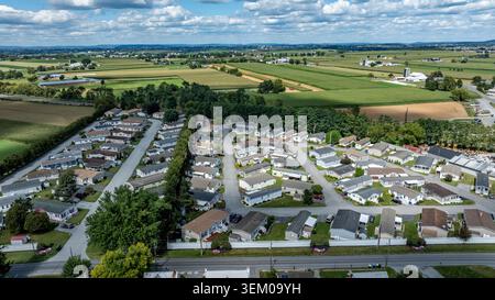 Die Szene zeigt eine Wohngegend mit mobilen, gefertigten Häusern, die in Reihen angeordnet sind. Im Hintergrund gibt es Felder und Hügel. Der Himmel ist klar mit Wolken. Das Land erscheint flach und grün. Stockfoto