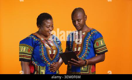 Ethnische Personen, die auf Social-Media-Webseiten navigieren, Nachrichten überprüfen und Fotos vor orangefarbenem Hintergrund ansehen. afroamerikanische Männer und Frauen, die Online-Websites im Studio scrollen. Stockfoto
