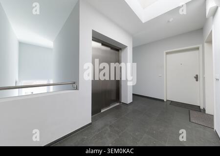 Innenarchitektur eines hellen und modernen Wohngebäudes mit schlanken Aufzugstüren aus Edelstahl, weißen Eingangstüren für Wohnungen, Stockfoto