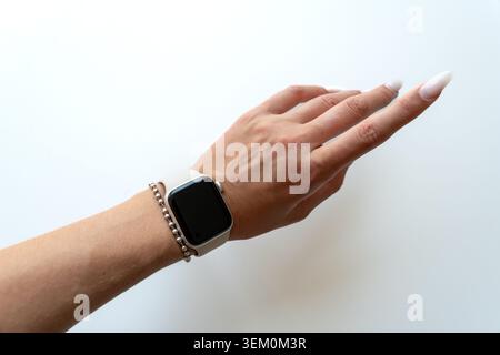 Weibliche Hand mit einer Smartwatch mit eleganter weißer Maniküre auf weißem Hintergrund, elegantem Casual-Stil, Platz für Text oder Produktplatzierung Stockfoto