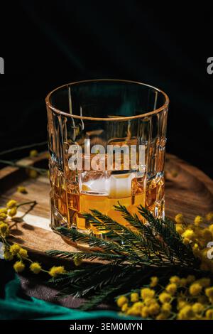 Whiskey mit Eis in Kristallglas und Mimosa Flowers elegantes Frühlingsgetränk Stockfoto