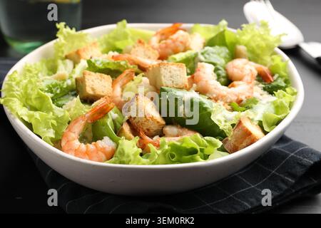 Leckerer Caesar-Salat mit Garnelen auf schwarzem Holztisch, Nahaufnahme Stockfoto