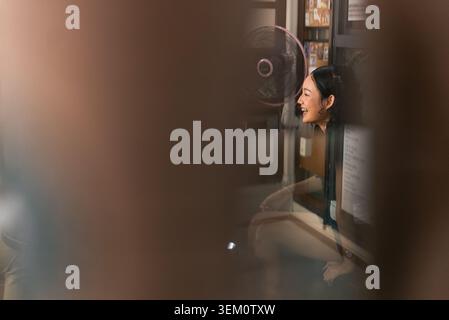 Junge asiatische Frau lächelt und lacht durch ein Fenster und erlebt Glück Stockfoto