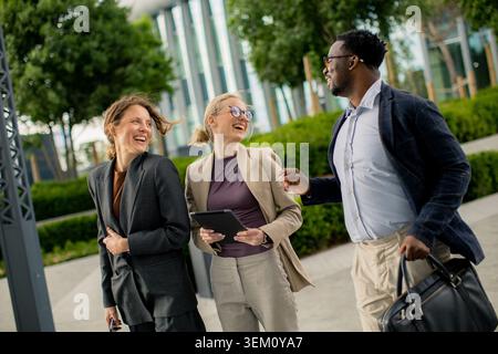 Drei Profis laufen zusammen in einem Stadtpark. Sie lächeln und führen Gespräche. Bäume und Stadtgebäude stehen im Hintergrund. Die Sonne ist Sch Stockfoto