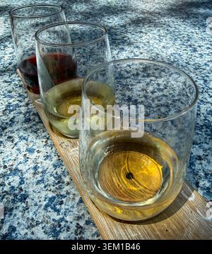 Nahaufnahme eines 3-Glas-Weinverkostungsflugs in stiellosen Weingläsern auf einem rustikalen Holzbrett. Stockfoto