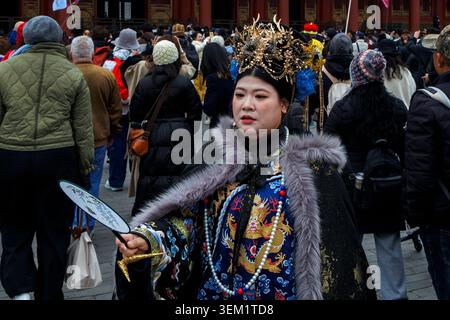 Eine Frau in farbenfroher traditioneller Kleidung hält einen Ventilator, während sie inmitten einer großen Menschenmenge steht, Verbotene Stadt, Peking, China Stockfoto
