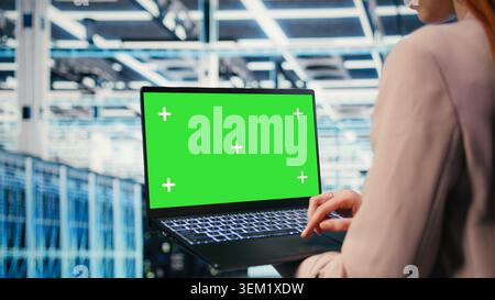Green-Screen-Laptop, der von weiblichen Softwareentwicklern für Rechenzentren zur Verwaltung von Cloud-Computing-IT-Lösungen in Unternehmen mit Laptop verwendet wird. Frau, die ein Modell-Notebook benutzt, um die Serverfarm zu überwachen, Kamera A Stockfoto