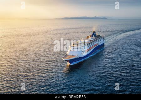 Aus der Vogelperspektive einer Kreuzfahrt oder eines Passagierschiffs, das über das ruhige Meer in den goldenen Sonnenuntergang segelt, mit Kopierraum Stockfoto