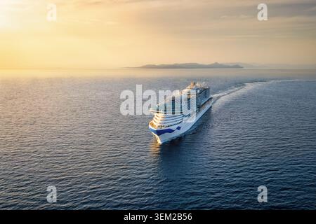 Aus der Vogelperspektive einer Kreuzfahrt oder eines Passagierschiffs, das über das ruhige Meer in den goldenen Sonnenuntergang segelt, mit Kopierraum Stockfoto