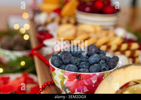 Makrofokus auf eine mit frischen Heidelbeeren gefüllte Blumenkeramik-Schüssel auf einem Weidebrett mit verschwommenem Hintergrund. Stockfoto