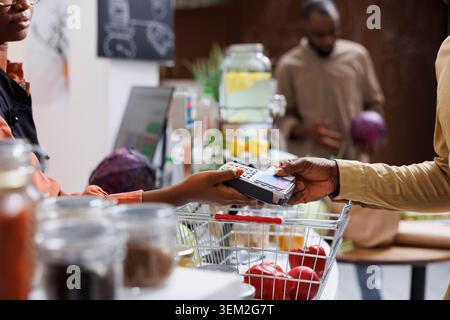 Detailbild eines afroamerikanischen Kunden, der am Checkout-Schalter mit einer Debitkarte bezahlt. Nahaufnahme einer Verkäuferin, die die POS-Maschine hält, damit der Kunde bezahlt. Stockfoto