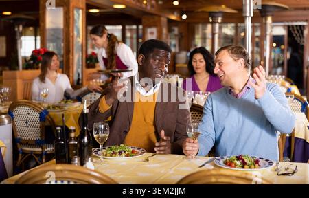 Zwei männliche Freunde trinken Wein und unterhalten sich im Restaurant Stockfoto