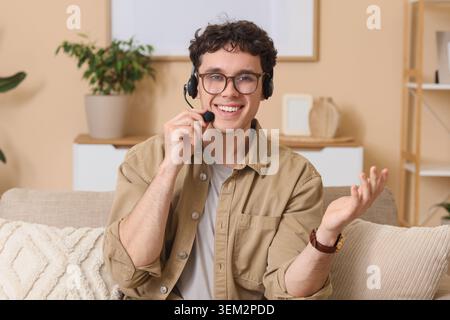 Junger männlicher Online-Unternehmensberater mit Headset, der zu Hause auf dem Sofa sitzt Stockfoto