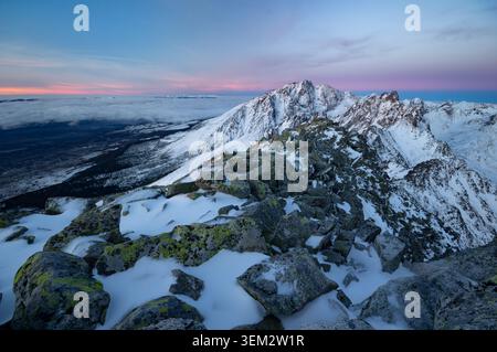Blick auf den schneebedeckten Slawkowski-Stit-Gipfel und den felsigen Bergrücken unter einem rosa Sonnenuntergang in Vysoke Tatry, Presowski kraj, Slowakei. Stockfoto