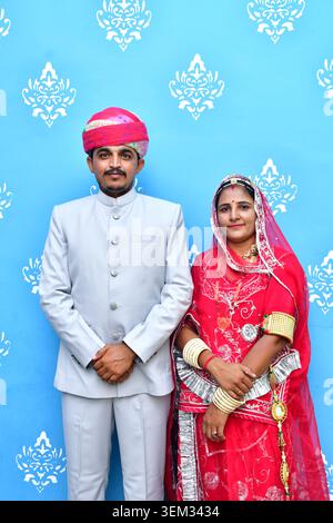 Wunderschönes indisches Paar in traditioneller Kleidung mit dem Mann in rosa Safa (Turban), der vor blauem Hintergrund posiert. Stockfoto