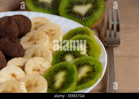 Nahaufnahme von Bananen- und Kiwis-Scheiben auf weißem Teller, symbolisiert gesunde Ernährung, Ernährung und farbenfrohe Fruchtpräsentation Stockfoto