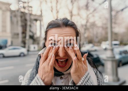 Frau, die im Herbst auf einem städtischen Bürgersteig steht, laut schreiend und mit aufgeregtem Ausdruck Stockfoto
