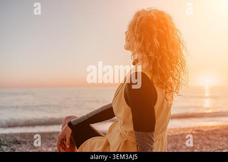 Frau Sonnenuntergang Strand, der während der goldenen Stunde am Ufer sitzt und das Meer mit Platz für Text beobachtet Stockfoto