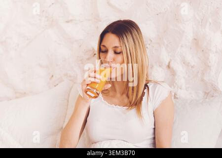 Junge Frau Trinkt Frischen Orangensaft Im Bett, Entspannendes Wellness-Konzept Zu Hause Stockfoto