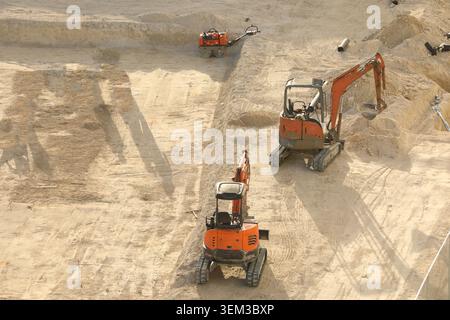 Orange Doosan Minibagger mit kompakter Raupenkette, die auf einer Sandbaustelle arbeiten und den Boden für Fundamente vorbereiten. Stockfoto