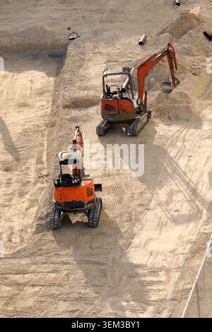 Orange Doosan Minibagger mit kompakter Raupenkette, die auf einer Sandbaustelle arbeiten und den Boden für Fundamente vorbereiten. Stockfoto