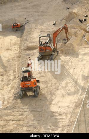 Orange Doosan Minibagger mit kompakter Raupenkette, die auf einer Sandbaustelle arbeiten und den Boden für Fundamente vorbereiten. Stockfoto