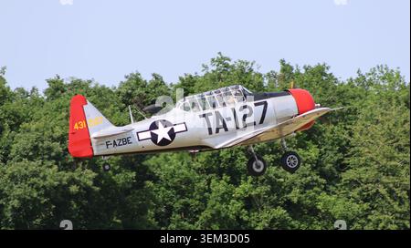 Ansicht eines alten texanischen T-6-Flugzeugs aus Nordamerika mit US-Militärmarkierungen, die tief über grüne Bäume fliegen, in La Ferte-Alais, Ile-de-France, Frankreich. Stockfoto