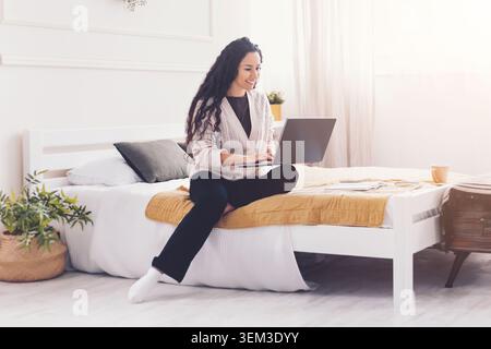 Glückliche Junge Frau, Die Am Laptop Arbeitet, Während Sie Zu Hause Auf Dem Bett Sitzt, Business-Konzept Stockfoto