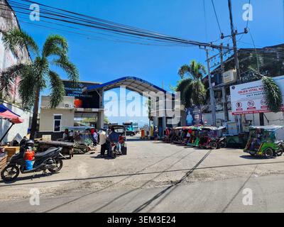 Makassar, Indonesien - 09. Februar 2024: Eingangstor des Paotere-Hafens mit geparkten dreirädrigen Rikschas (Becak) unter blauem Himmel. Stockfoto