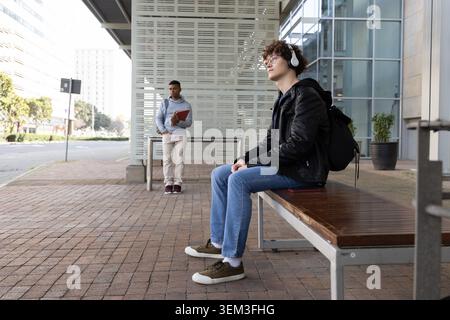 Verschiedene männliche Teenager-Studenten warten an der Notbank mit Headset, halten roten Ordner, Kopierraum Stockfoto