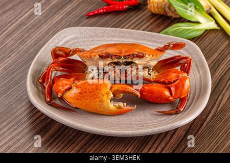 Köstliche gedämpfte Orangen-Wildkrabben serviert auf einem Keramikteller. Umgeben von roten Chilischoten, Pak Choy und Ingwer auf einem Holztisch. Perfekt für das Meer Stockfoto