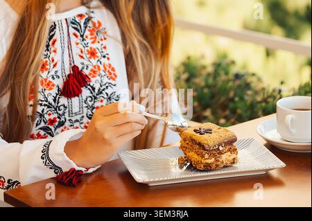 Köstliches Dessert serviert auf Teller mit Gabel in der Hand im Café am Nachmittag. Das Mädchen hält die Gabel bereit, um einen Happen vom Dessert auf einem blau gemusterten Teller zu nehmen Stockfoto