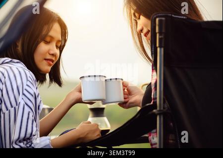 Asiatische junge zwei Frauen, die sitzen, genießen die Zubereitung von Tropfkaffee in der Nähe eines Campingzelt, Kaffeegetränk entspannend in den morgendlichen Sommerurlaub. Stockfoto