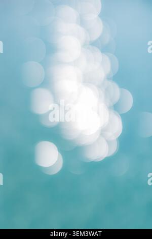 Glitzernde Wasseroberfläche mit weichem Bokeh-Licht auf türkisfarbenem Meer, abstrakte Natur. Schimmernde Meeresdetails. Sommerhintergrunddesign, Kopierraum vertikal Stockfoto