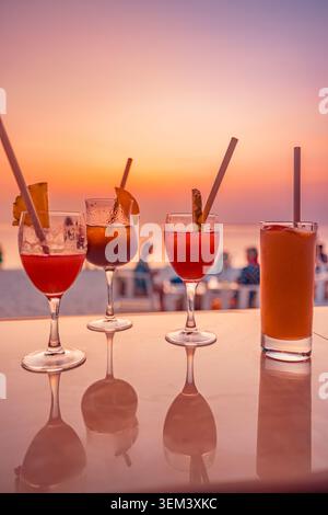 Strandcocktails in Gläsern auf der Bar mit tropischem Sonnenuntergang am Meer und Menschen im Hintergrund. Sommerurlaub-Getränke-Resort. Cocktail-Strandurlaub-Reiseparadies Stockfoto