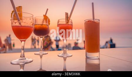 Bunte Sommer-Cocktails auf der Theke einer tropischen Strandbar bei Sonnenuntergang mit Menschen. Party mit Urlaubstrinken am Meer. Cocktail-Strandurlaub-Reise-Resort bei Sonnenuntergang Stockfoto
