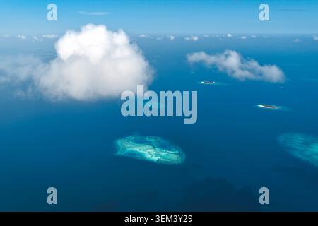 Aus der Vogelperspektive auf tropische Inseln und Korallenriffe, die über den tiefblauen Indischen Ozean unter flauschigen weißen Wolken in Kudahuvadhoo, Dhaalu Atoll, M, verstreut sind Stockfoto