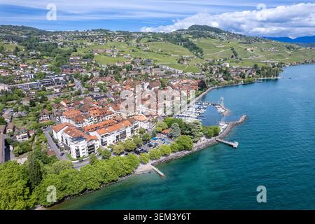 Aus der Vogelperspektive auf die historische Stadt Lutry mit ihren roten Dächern und dem Hafen am Ufer des Genfer Sees unter blauem Himmel in Lutry, Waadt, Schweiz. Stockfoto