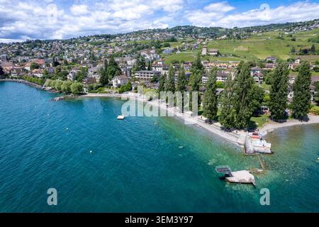 Blick aus der Vogelperspektive auf die Stadt Lutry am Ufer des Genfer Sees mit üppigen Weinbergen, Wohnhäusern am Hügel und hohen Bäumen am Wasser Lutr Stockfoto