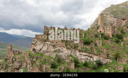 Weite Landschaft Blick auf die verlassenen Steindorfruinen von Kahib auf einem steilen felsigen Hügel in Dagestan, Russland, mit mittelalterlichen Turmhäusern und bewölktem Himmel Stockfoto