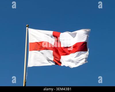 Die englische Flagge des St. George's Cross fliegt vom Fahnenmast aus und zeigt das weiße und rote Kreuz vor dem Hintergrund des blauen Himmels in England Stockfoto