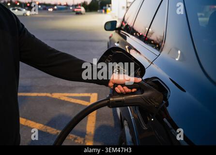Nahaufnahme eines Mannes, der nachts ein Ladegerät an ein Elektroauto anschließt Stockfoto