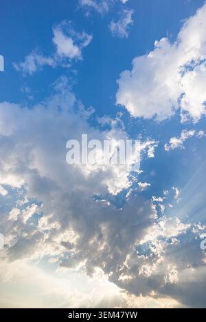 Blaue-Himmel-Sonnenstrahlen, weiße Wolken, Sonnenlichtstrahlen, heller, friedlicher Tageshimmel, vertikal. Sommer-Natur-Himmel-Hintergrund. Tapetenhintergrund-Wandkunst Stockfoto