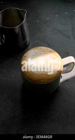 Licht und Schatten auf einer Kaffeetasse gefüllt mit Cappuccino, dunkler Tischhintergrund Stockfoto